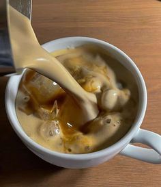 a spoon full of soup being poured into a white cup on a wooden table top