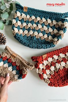 three crocheted purses sitting on top of a white table next to a pine cone