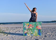 a woman standing on the beach with her arms in the air