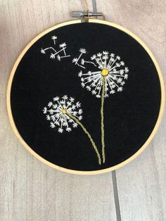 a black and white embroidery with dandelions in it on a wooden table top