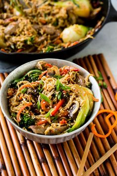 a bowl filled with stir fry vegetables on top of a bamboo mat next to an orange pair of chopsticks