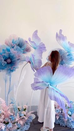 a woman is standing in front of flowers with blue and pink petals on her wings