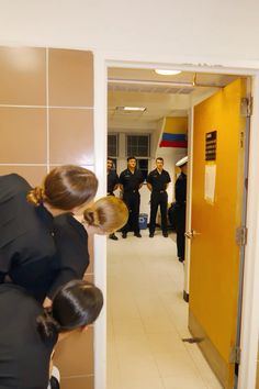 two women in business attire are looking into a hallway with other people standing behind them