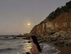 a woman walking on the beach at night with her child in front of him and full moon rising over the ocean