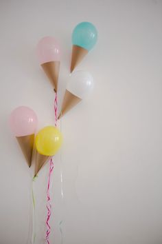 three ice cream cones with balloons tied to them on a white wall, one is pink and the other is blue