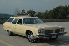 a beige station wagon parked in a parking lot with two people sitting on the roof