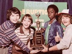 four young people holding up a trophy and giving the thumbs up in front of a banner