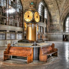 there is a large clock in the middle of a building with benches and tables around it