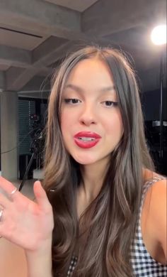 a woman with long brown hair and red lipstick holding her hand up to the camera