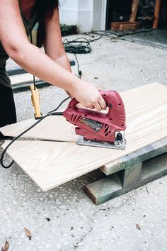 a woman sanding up some wood with a power tool on top of the board