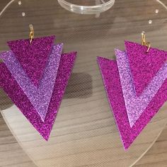 purple and pink glittered triangle shaped earrings on clear acrylic