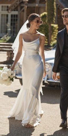 a woman in a wedding dress walking down the street with a man holding a bouquet