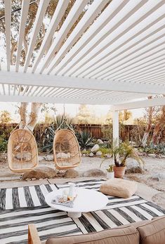 an outdoor living area with two hanging chairs and a table on top of a black and white striped rug