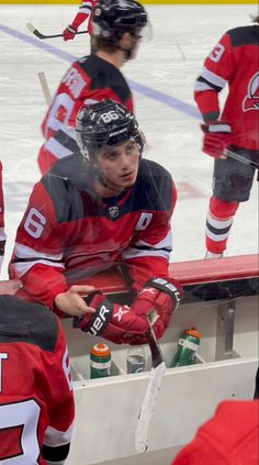 a hockey player sitting on the bench in front of his teammates and talking to each other