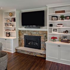 a living room with white shelves and a fireplace in the center, along with a flat screen tv mounted above it