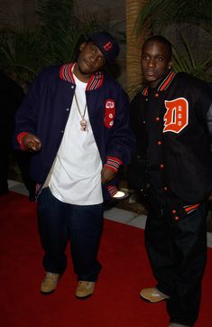 two men standing next to each other in front of a red carpeted area with palm trees