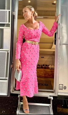 a woman in a pink dress is standing by the open door of a silver trailer