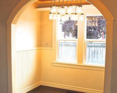 an empty room with wood flooring and a chandelier hanging from the ceiling