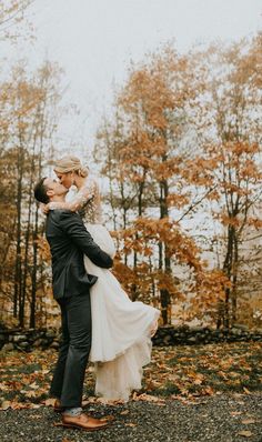 a bride and groom kissing in front of trees with leaves on the ground during their fall wedding