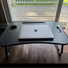 an apple laptop sitting on top of a black table in front of a sliding glass door