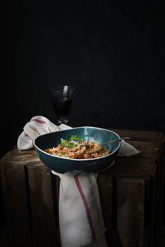 a bowl of food sitting on top of a wooden table next to a glass of wine