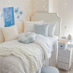 a white bed topped with pillows next to a night stand filled with books and lights