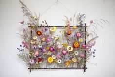 an arrangement of wildflowers and ferns hangs on a wall in front of a white wall