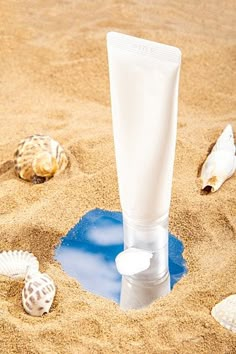 a tube of lotion sitting in the sand with seashells around it,