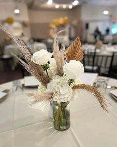 a vase filled with flowers and feathers on top of a white table cloth covered table