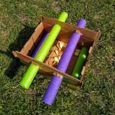 an open cardboard box filled with purple and green yoga mats on top of a grass covered field