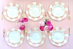 the table is set with pink and white plates, silverware, and flowers on them