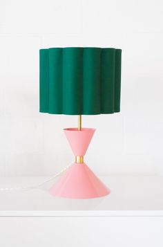 a pink table lamp with a green shade on the base and a white wall behind it