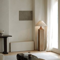 a living room with a couch, table and lamp on the floor in front of a window