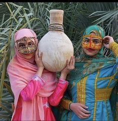 two women in colorful costumes holding up a vase