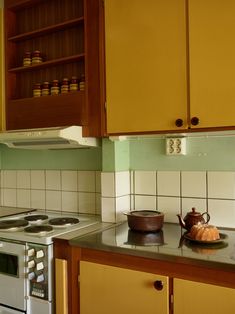 a kitchen with yellow cabinets and a tea pot on the stove top in front of an oven