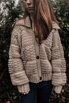 a woman standing in front of some bushes wearing a jacket with buttons on the side