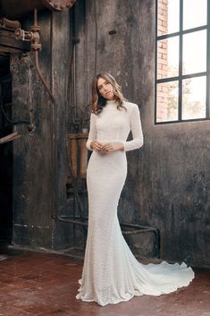 a woman in a white wedding dress standing next to a brick wall and industrial machinery