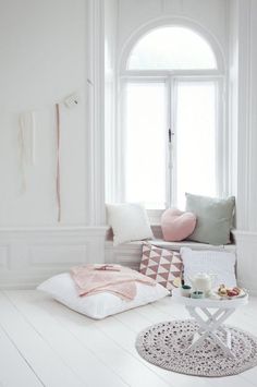 a living room with white walls and flooring is furnished with pillows, rugs and blankets