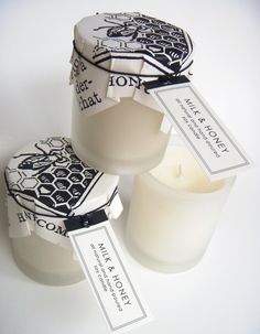 two white candles with labels on them sitting next to each other, one candle has been opened and the other is closed