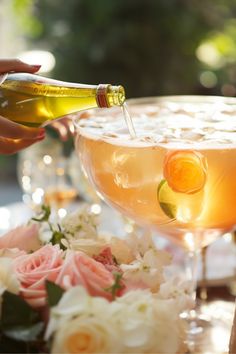 someone is pouring champagne into a glass with flowers on the table in front of them