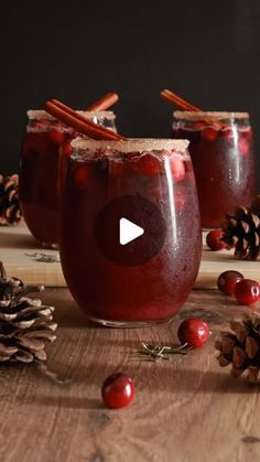 two glasses filled with cranberry punch sitting on top of a wooden table next to pine cones