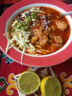 a bowl of soup with meat, cabbage and lemons on the table next to it