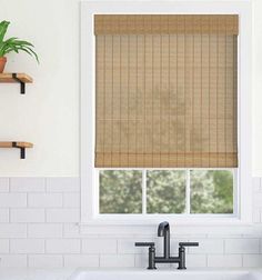 a kitchen sink under a window with a bamboo roman blind in the window above it