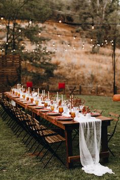 a long table with candles on it in the middle of an outdoor area, surrounded by string lights