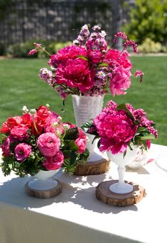 pink and red flowers in white vases sitting on top of a wooden slice table