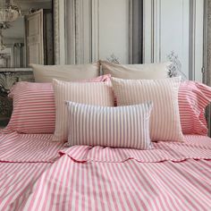 a bed with pink and white striped sheets, pillows and pillow cases on top of it