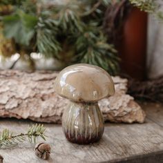 a glass mushroom sitting on top of a wooden table next to pine cones and branches