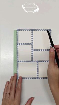 two hands are holding scissors over a piece of paper with squares and lines on it