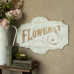 a white flower shop sign sitting on top of a shelf next to a vase with flowers