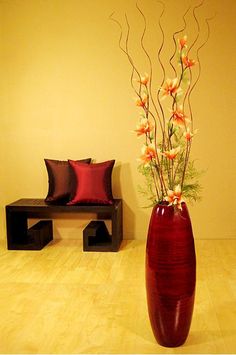 a large vase with flowers in it sitting on the floor next to a small bench